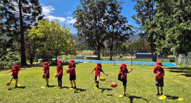 Group of students kicking a football on grassy area